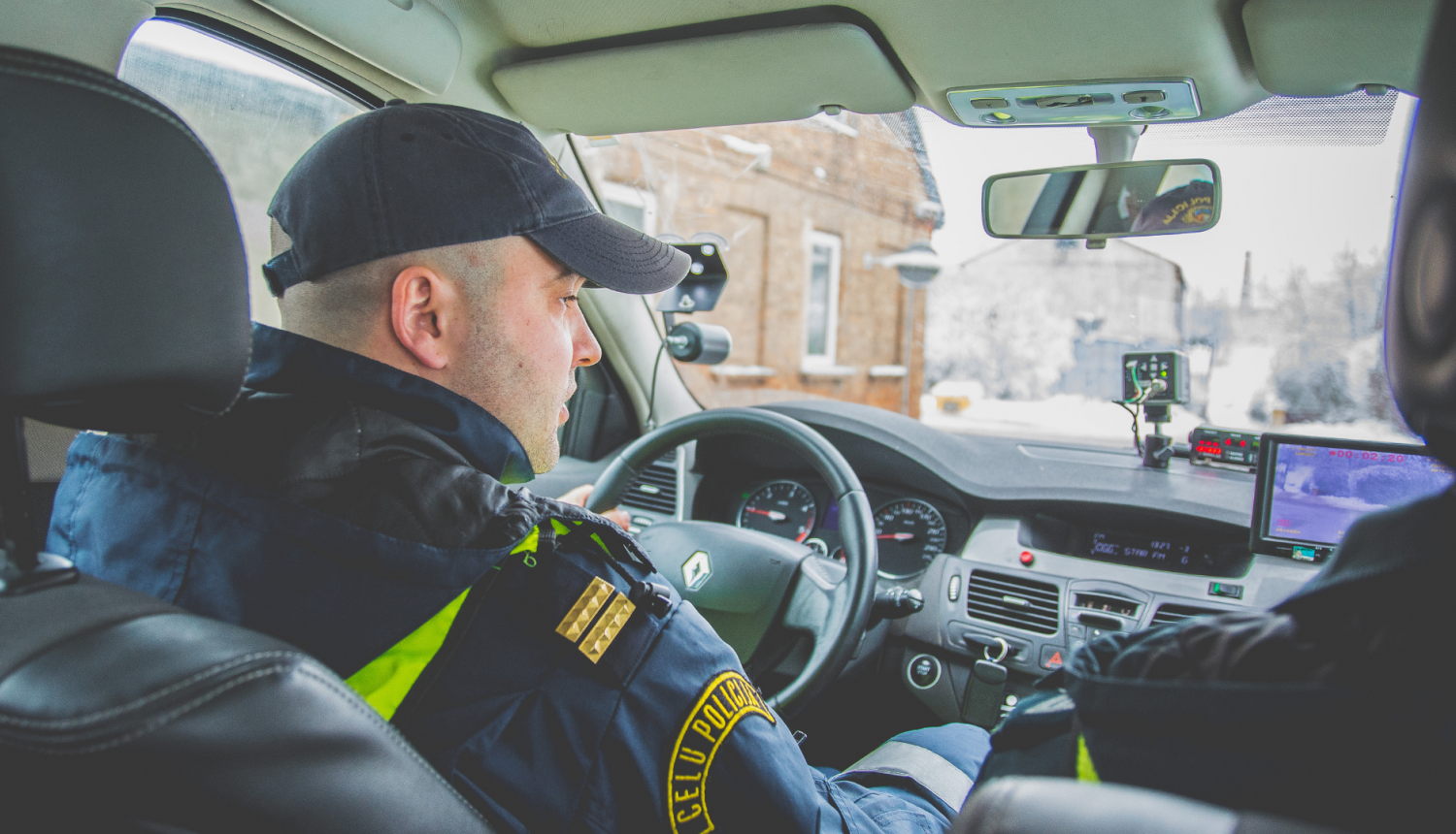 Ceļu policijas darbinieks automašīnā pie stūres, fotografēts no aizmugurējās sēdvietas