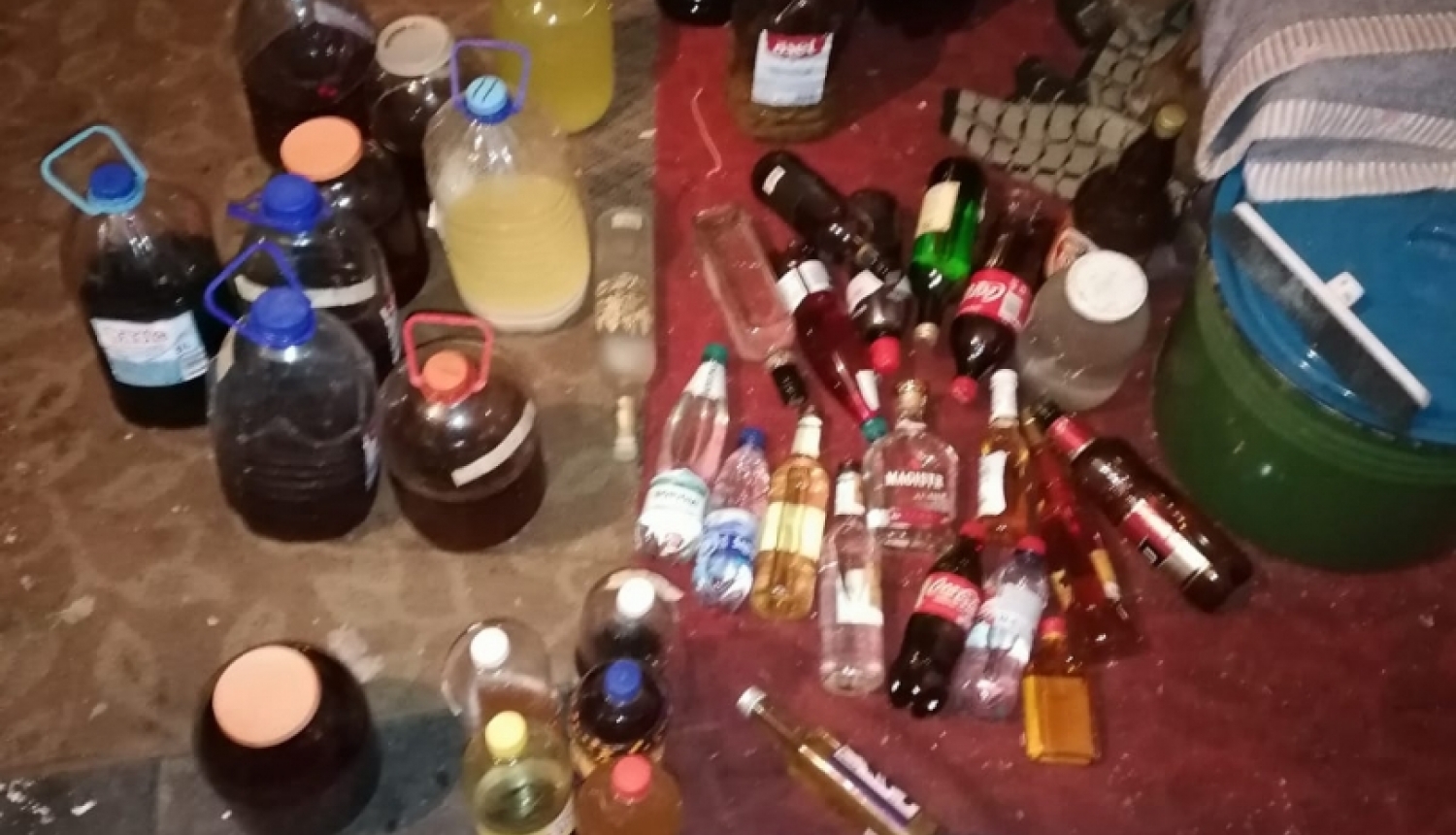 Uz grīdas redzamas dažāda tilpuma pudeles ar dažādas krāsas nelikumīgu alkoholu